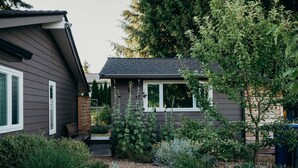 Ein Wohnhaus mit Vorgarten, einer kleinen Veranda und einem Garten mit verschiedenen Pflanzen und Sträuchern.