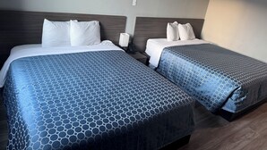 A hotel room with two beds, each with a blue patterned bedspread and white pillows. There is a bedside table with a lamp and a phone on it. - Champion Inn (Shepherd)
