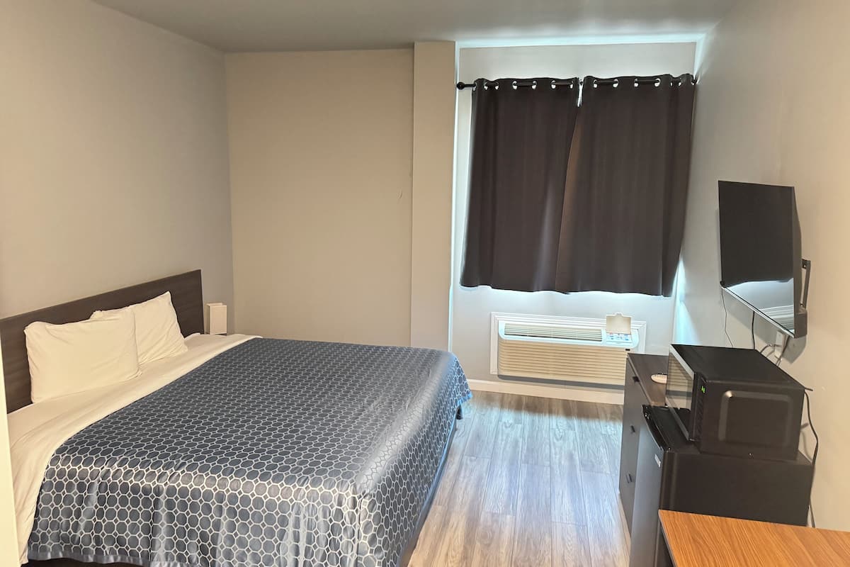 Habitación de hotel con cama, escritorio, silla, ventana con cortinas y televisor montado en la pared.