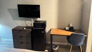 A small office space with a desk, a chair, a television, a microwave, and a trash can. - Champion Inn (Shepherd)