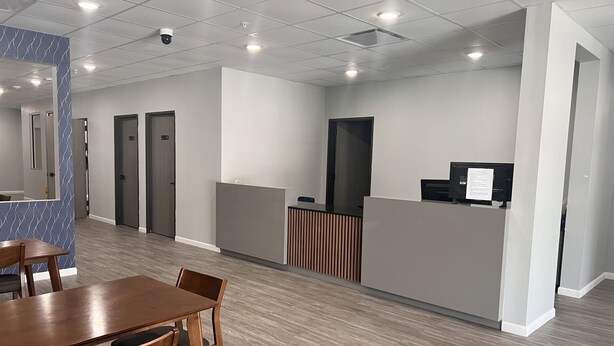 A modern reception area with a wooden reception desk, a seating area with a table and chairs, and a patterned wall. - Champion Inn (Shepherd)