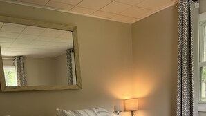 A neatly made bed with striped bedding, a bedside lamp, and a mirror on the wall. - 
Maple Street Cottage is the perfect couple’s retreat. (Lake)