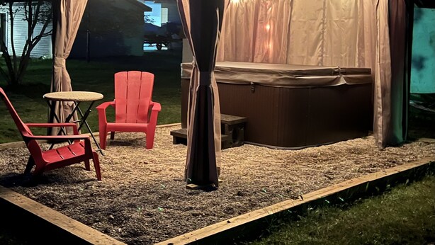A covered outdoor seating area with string lights, a hot tub, and red chairs. - 
Maple Street Cottage is the perfect couple’s retreat. (Lake)