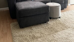 A living room with a grey sectional sofa, a small ottoman, and a 'HAPPY' pillow. - 
Maple Street Cottage is the perfect couple’s retreat. (Lake)