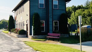 A two-story building with a dark blue exterior, a central chimney, and a small porch area with a bench. - 
Maple Street Cottage is the perfect couple’s retreat. (Lake)