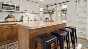 A modern kitchen with white cabinets, a central island with stools, a stainless steel oven, and a hanging rack. - Steps From the Beach. Tahoe Tipsy Trout. It's a VIBE (Kings Beach)