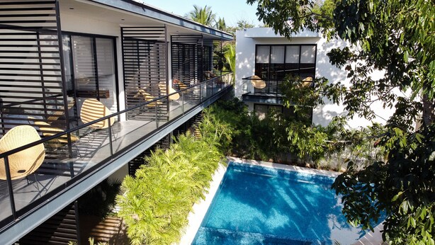 Una casa moderna con un balcone in vetro affacciato su una piscina, immersa nel verde.