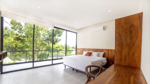 Camera da letto moderna con una grande finestra, un letto, una scrivania in legno e vista sugli alberi.