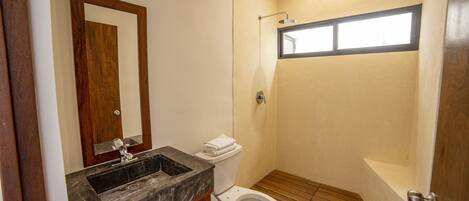 A bathroom with a wooden vanity, a white toilet, a shower with a window, and a bathtub.