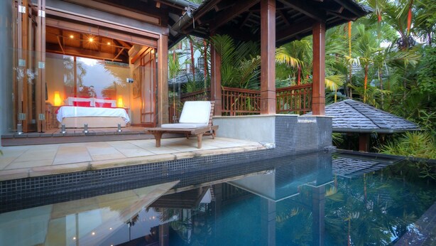 A modern pool area with a lounge chair and a bed visible through a glass door.