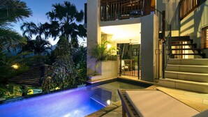 A pool area with a staircase leading to a balcony, surrounded by tropical plants.