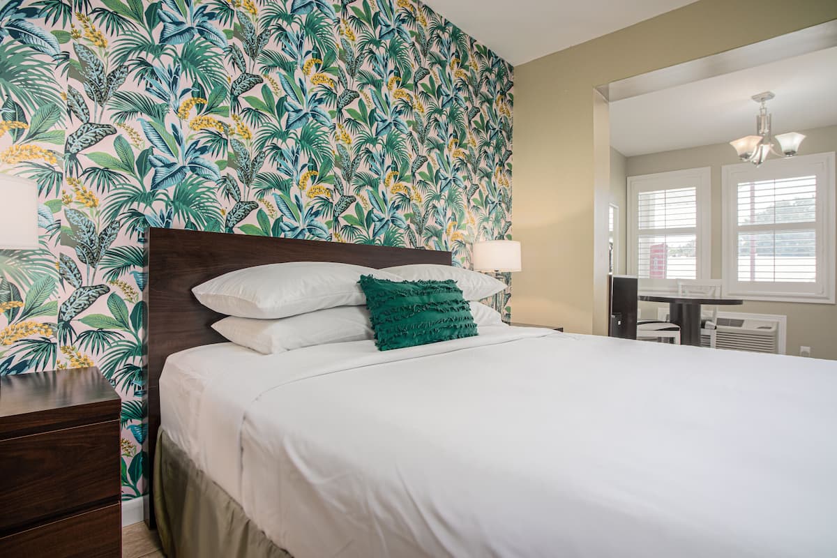 Une chambre d’hôtel avec un lit, une table de chevet, une lampe et une fenêtre avec des stores.