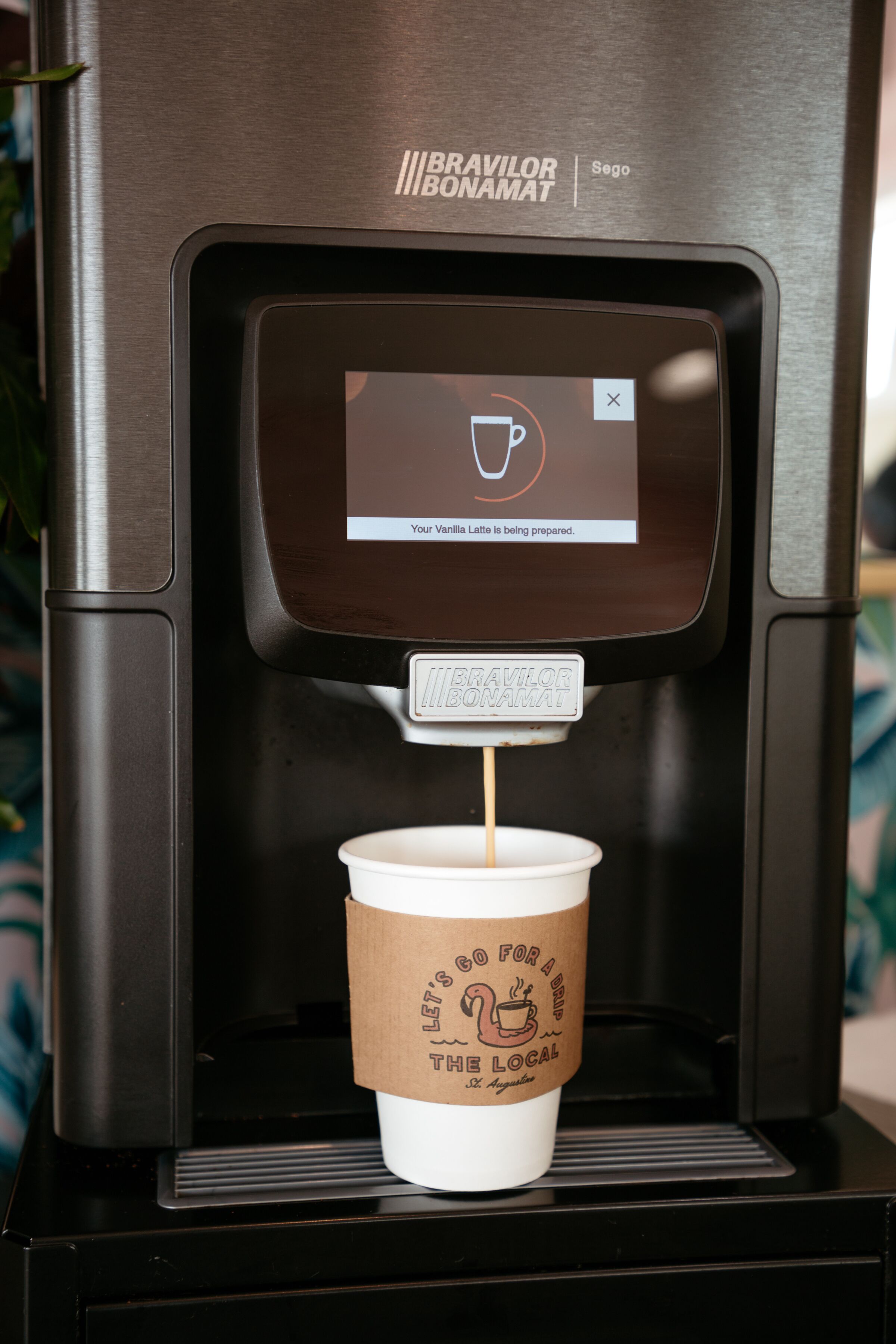 A coffee machine with a digital display indicating a latte is being prepared.