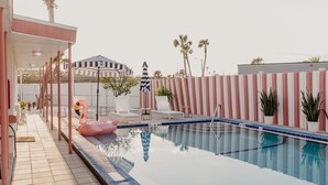 A swimming pool with lounge chairs and a flamingo float, surrounded by a striped fence and palm trees. - The Local - St. Augustine (St. Augustine)