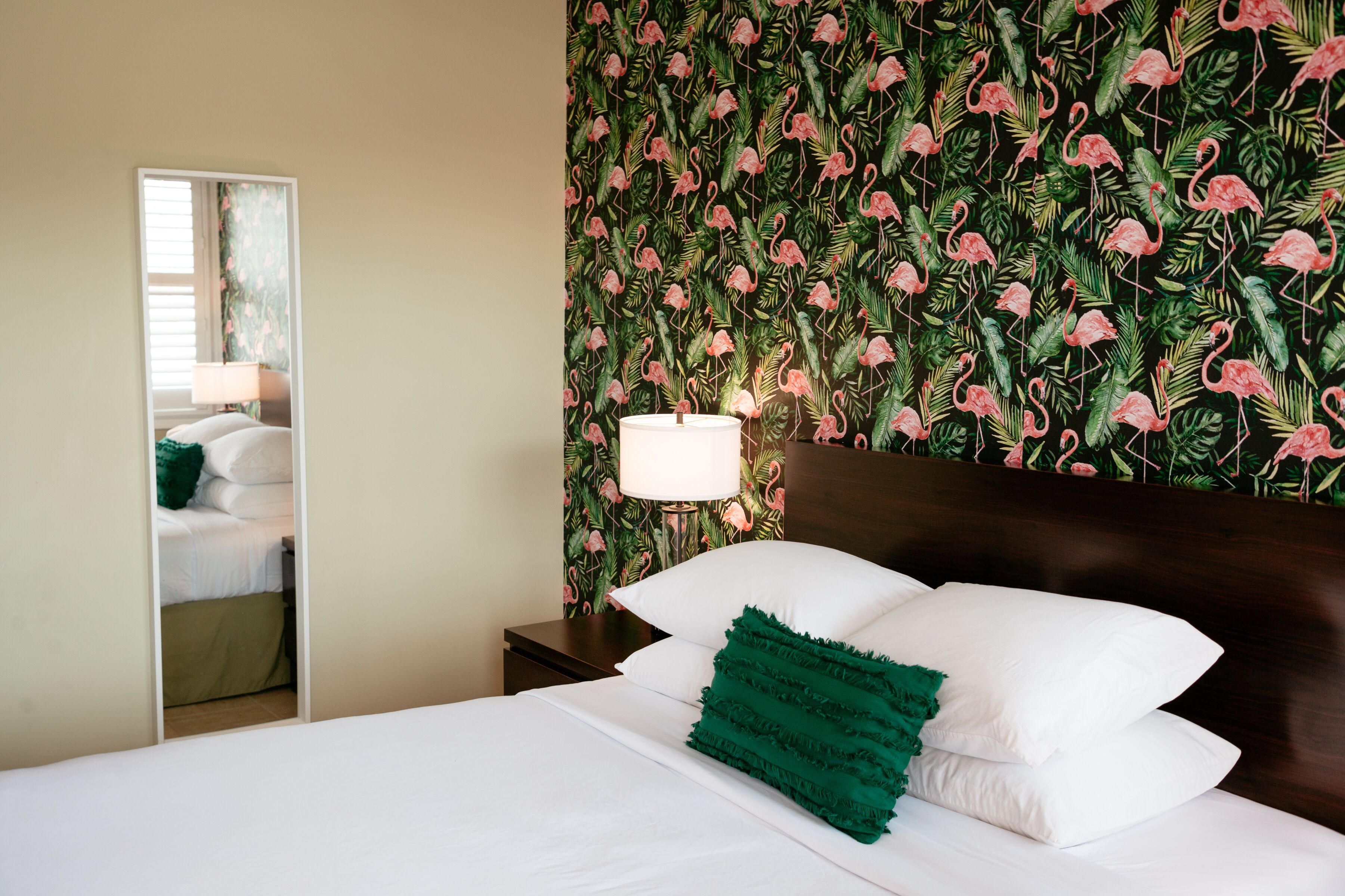 A hotel room with a bed, a nightstand, a lamp, and a mirror.