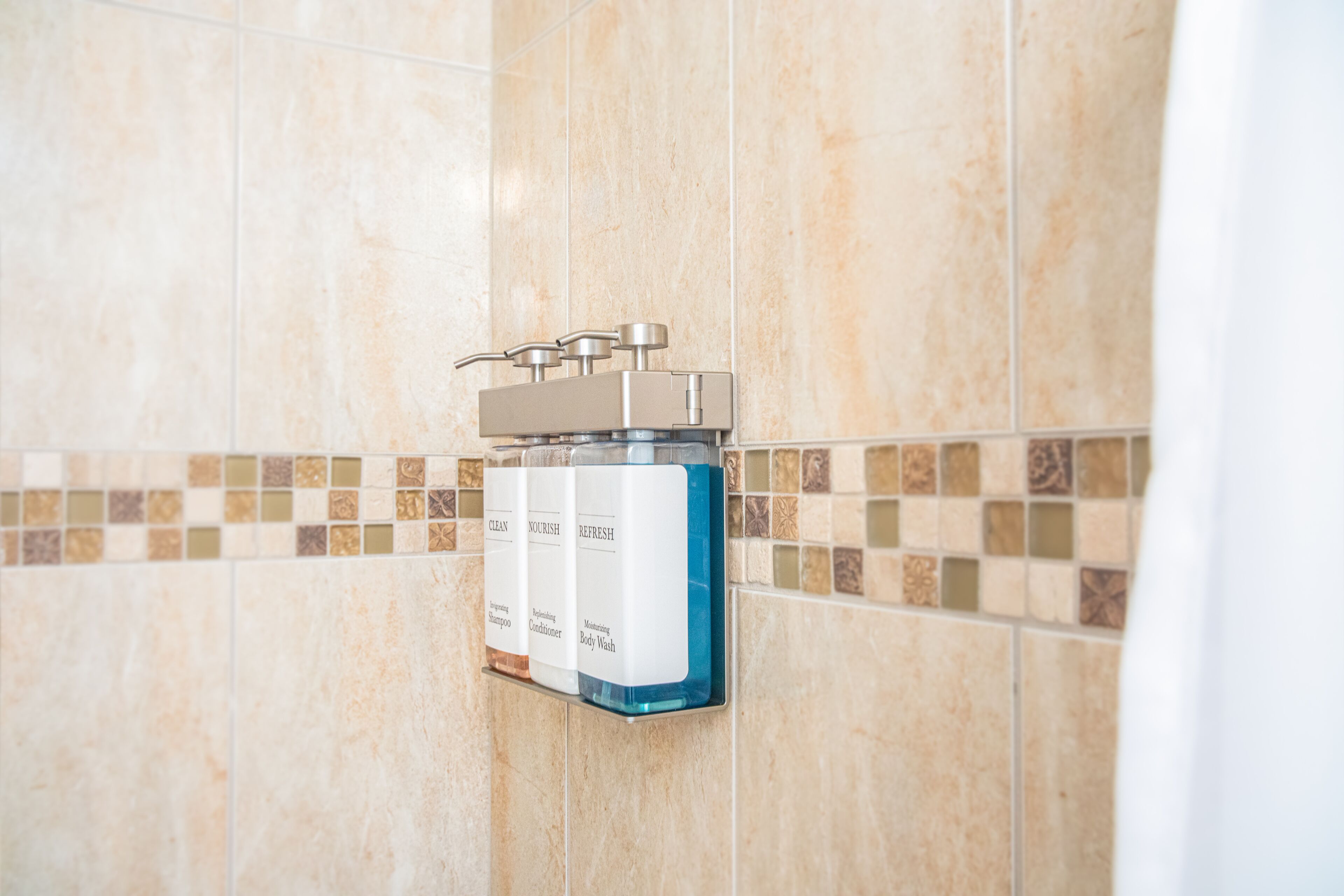 A bathroom with a wall-mounted soap dispenser and a tiled backsplash.