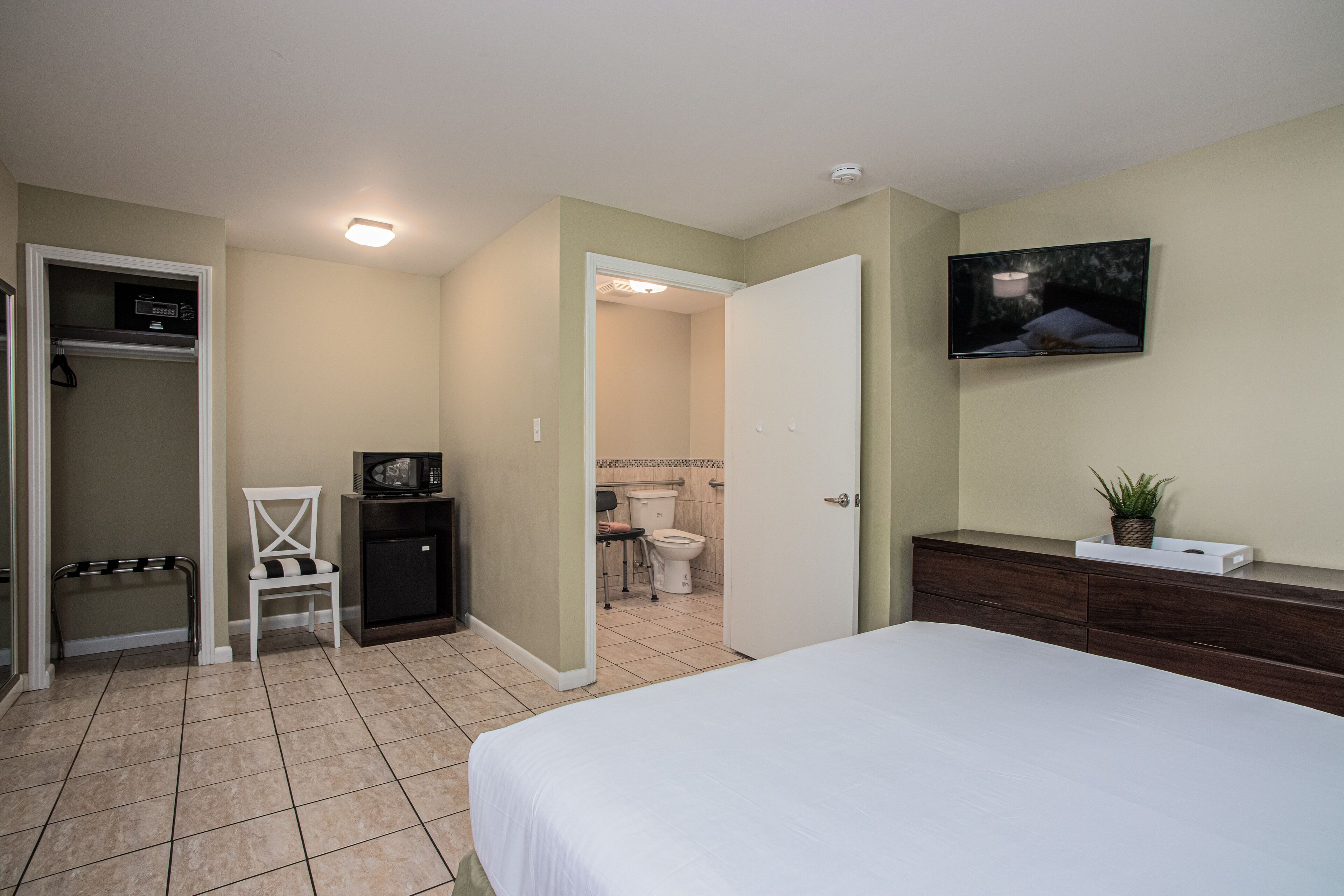 Une chambre à coucher avec un lit, un téléviseur fixé au mur, une commode et un placard.
