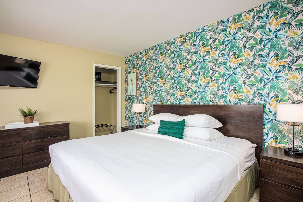 Une chambre d’hôtel avec un lit, un téléviseur fixé au mur, une armoire et une salle de bain visible à travers une porte ouverte.
