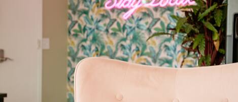 A room with a tufted headboard, a neon sign reading "Stay Local," and a wall with a tropical leaf pattern.