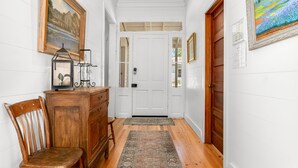 Un pasillo con un banco de madera, una pequeña mesa con lámpara y una puerta con panel de vidrio.