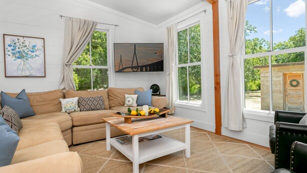 Una sala de estar acogedora con un sofá color beige, una mesa de centro de madera y un ventanal con vistas a la vegetación.