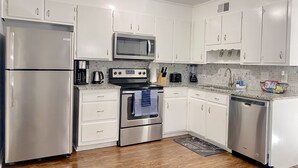 Cozinha moderna com eletrodomésticos de aço inoxidável, armários brancos e painel de azulejos.