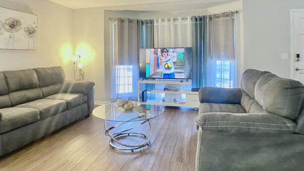 Uma sala de estar com dois sofás cinza, uma mesa de centro de vidro e uma TV de tela plana em um suporte.