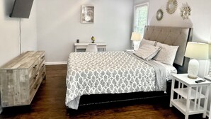 Quarto com cama, escrivaninha, cadeira, cômoda, ventilador de teto e decoração na parede.