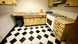 Een keuken met houten kastjes, een zwart-wit geruite vloer, een fornuis en een spoelbak.