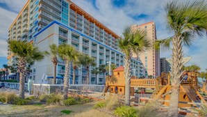 Un hôtel à plusieurs étages doté de balcons, de palmiers et d’un terrain de jeux.