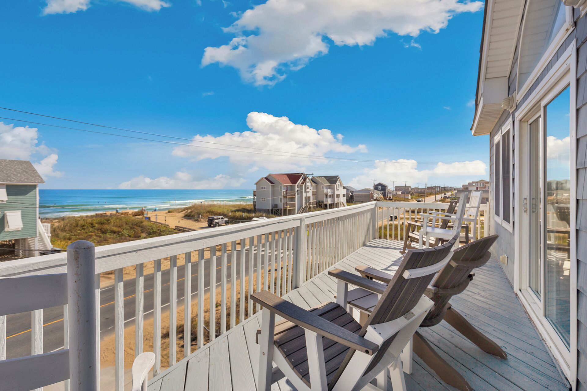 A wooden deck with chairs and a table overlooking a beach and ocean.