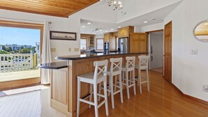A modern kitchen with wooden cabinets, a black countertop, and white bar stools. - Nautica Nook: Ocean Escape with Saltwater Pool (Corolla)