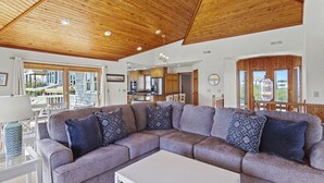 A modern living room with a sectional sofa, a white coffee table, and a wooden ceiling. - Nautica Nook: Ocean Escape with Saltwater Pool (Corolla)