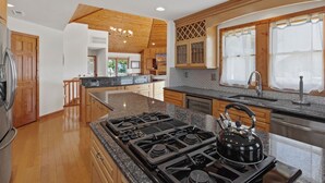 A modern kitchen with granite countertops, a gas stove, and wooden cabinetry. - Nautica Nook: Ocean Escape with Saltwater Pool (Corolla)