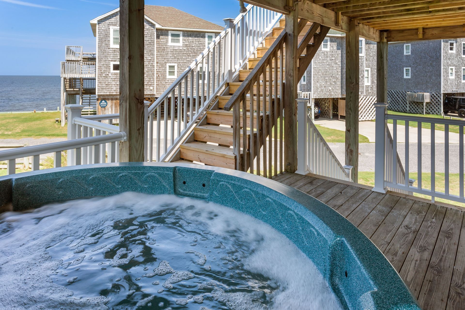 A wooden deck with a hot tub, a staircase, and a view of the ocean.
