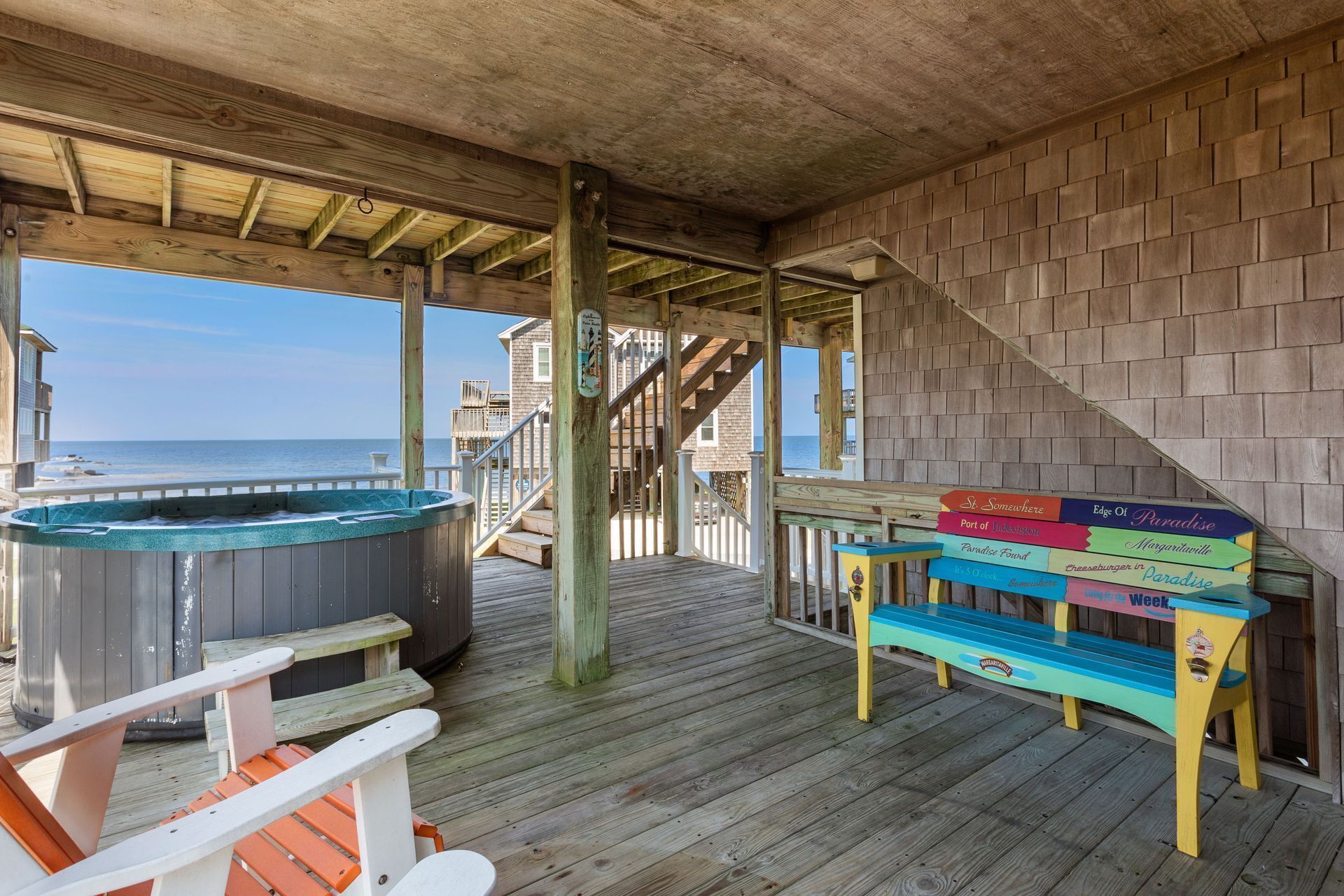 A wooden deck with a hot tub, a wooden staircase, and a colorful bench with signs.