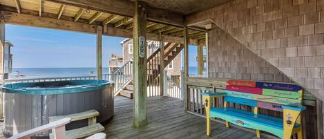 A wooden deck with a hot tub, a wooden staircase, and a colorful bench with signs.