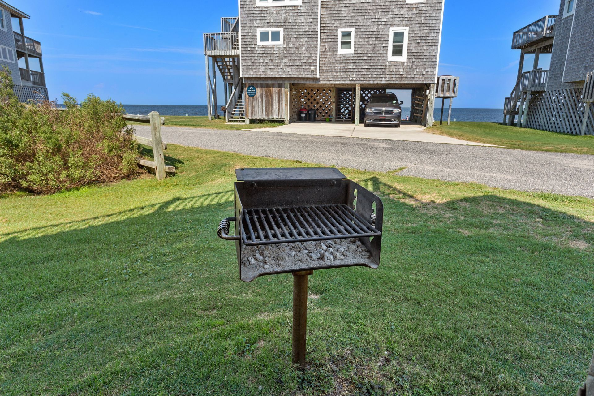 A barbecue grill in a grassy area with a wooden deck and a building in the background.
