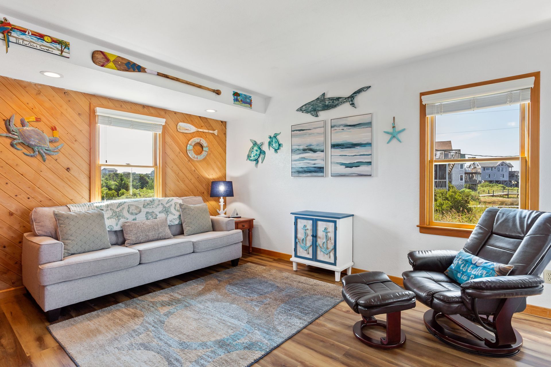 A living room with a wooden floor, a grey sofa, a leather recliner, a blue cabinet, and nautical-themed decorations.
