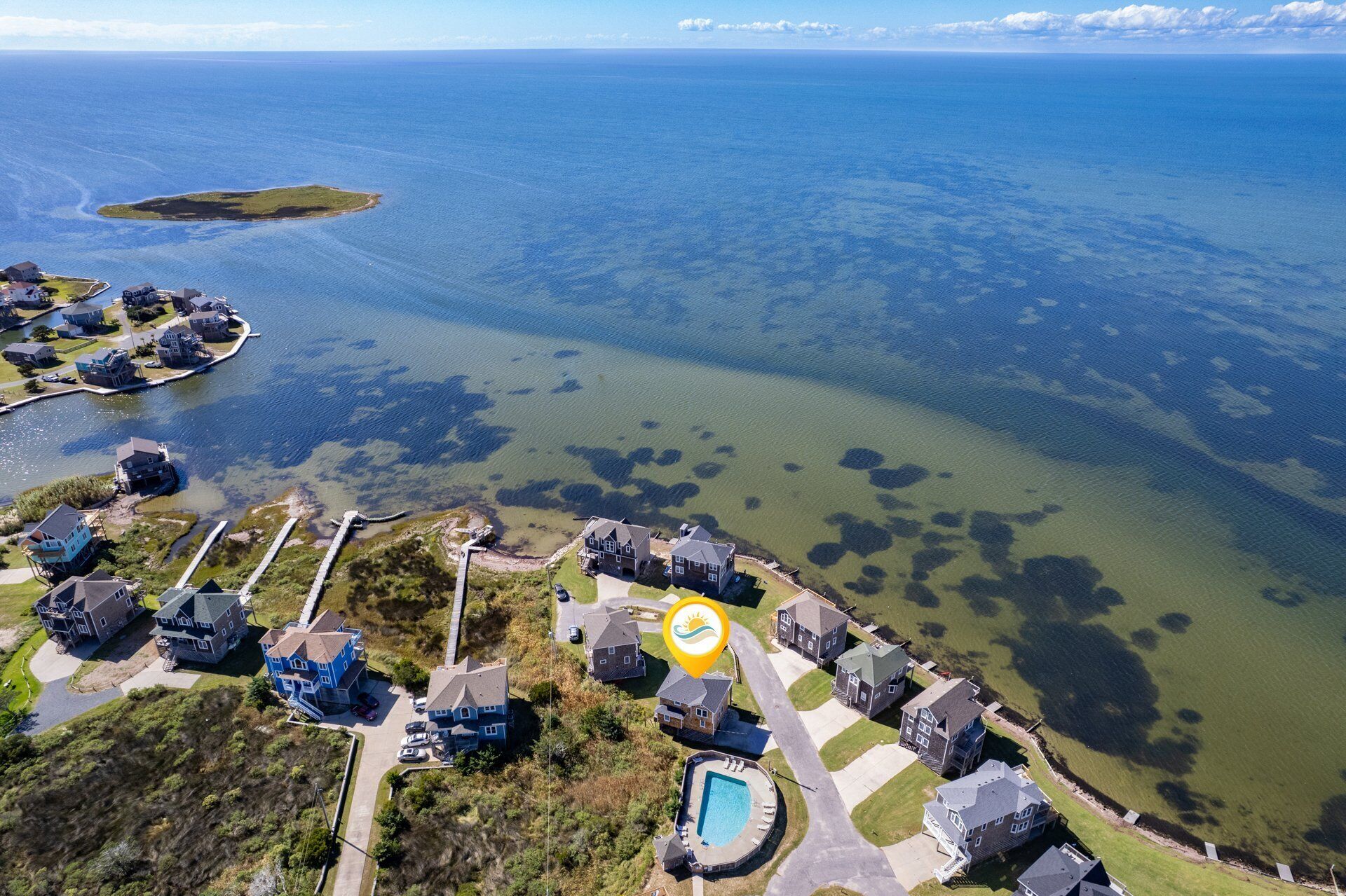 Vista aérea de una zona residencial costera con casas, una piscina y una vista despejada del océano.