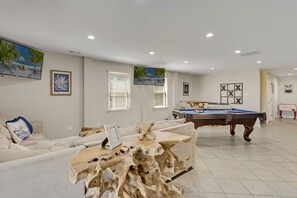 Ein geräumiges Wohnzimmer mit Billardtisch, einer Couch und einem Couchtisch mit einem besonderen Holzdesign.