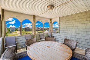 A covered patio with a round table and wicker chairs, large windows with a view of a residential area. - 7000 Serenity Sands*Pool*Dog Friendly*Pool Table (Nags Head)