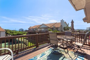 Eine Holzterrasse mit Gartenmöbeln, Blick auf ein Gebäude mit Satteldach und einem klaren, blauen Himmel.