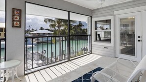 Un balcon donnant sur une marina, une table blanche et un ventilateur de plafond.