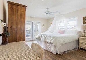 A bedroom with a bed under a canopy, a wooden wardrobe, a wicker chair, and a nightstand with a lamp. - Family & Pet-Friendly Duck Key Home – Heated Pool, 90’ Dock, Ocean Access (Duck Key)