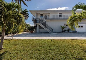 A two-story building with a central staircase, surrounded by a well-maintained lawn and palm trees. - Family & Pet-Friendly Duck Key Home – Heated Pool, 90’ Dock, Ocean Access (Duck Key)