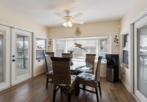 A dining area with a round glass table, wicker chairs, and a ceiling fan. - Family & Pet-Friendly Duck Key Home – Heated Pool, 90’ Dock, Ocean Access (Duck Key)