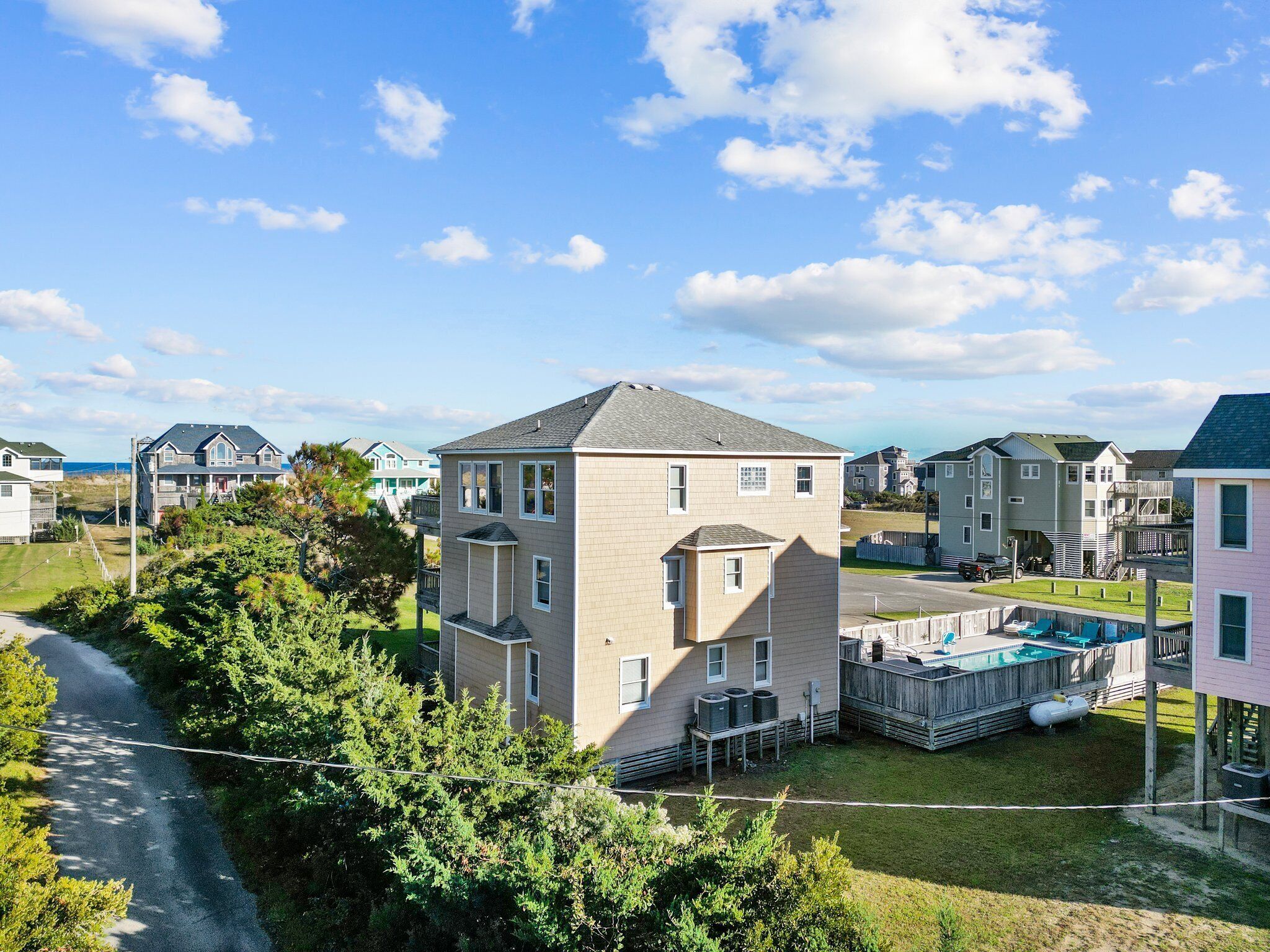 A residential area with a two-story house featuring a balcony, a swimming pool, and a view of the sea.