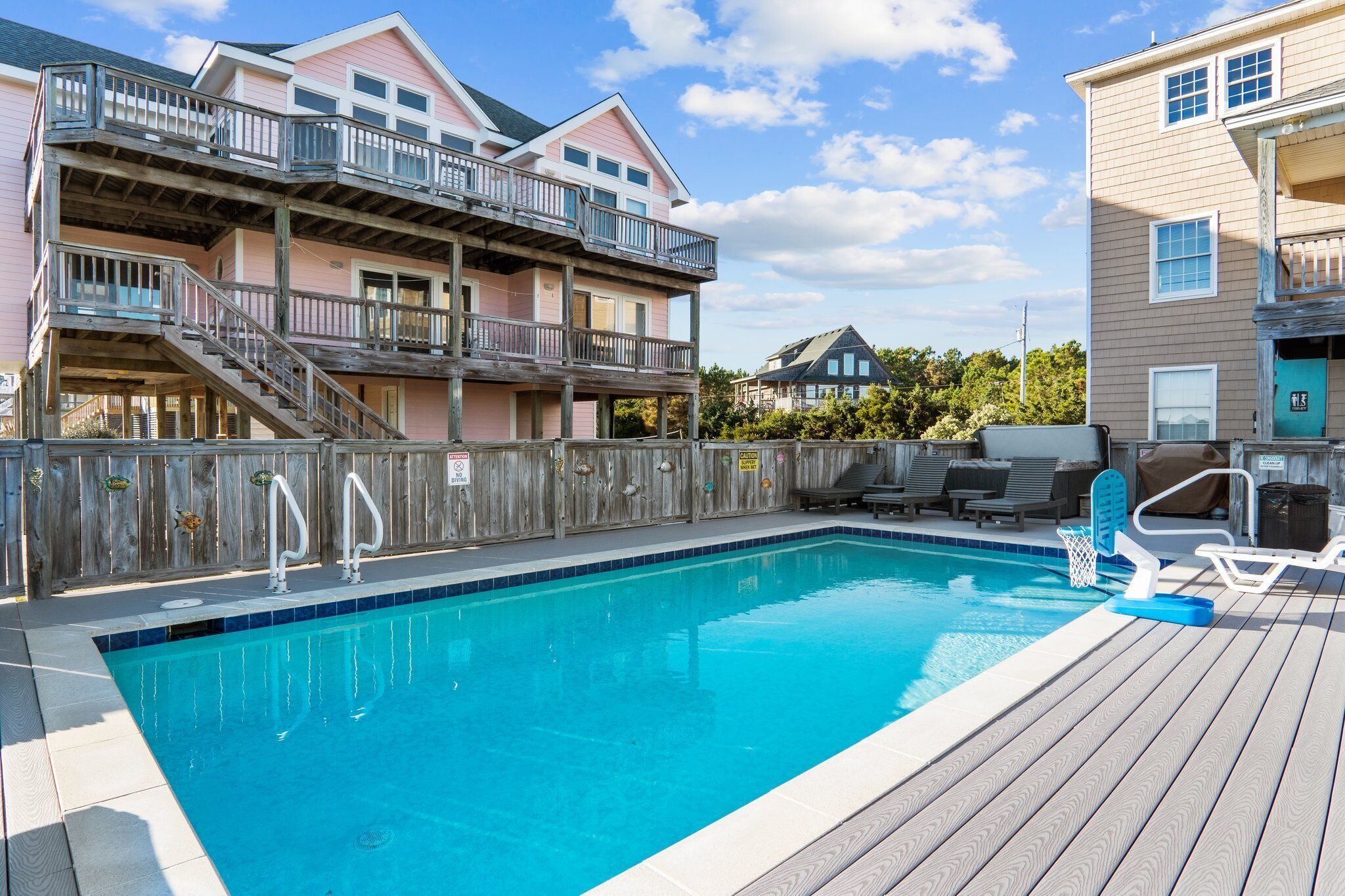 A swimming pool with a wooden deck, a wooden fence, and a building with balconies.