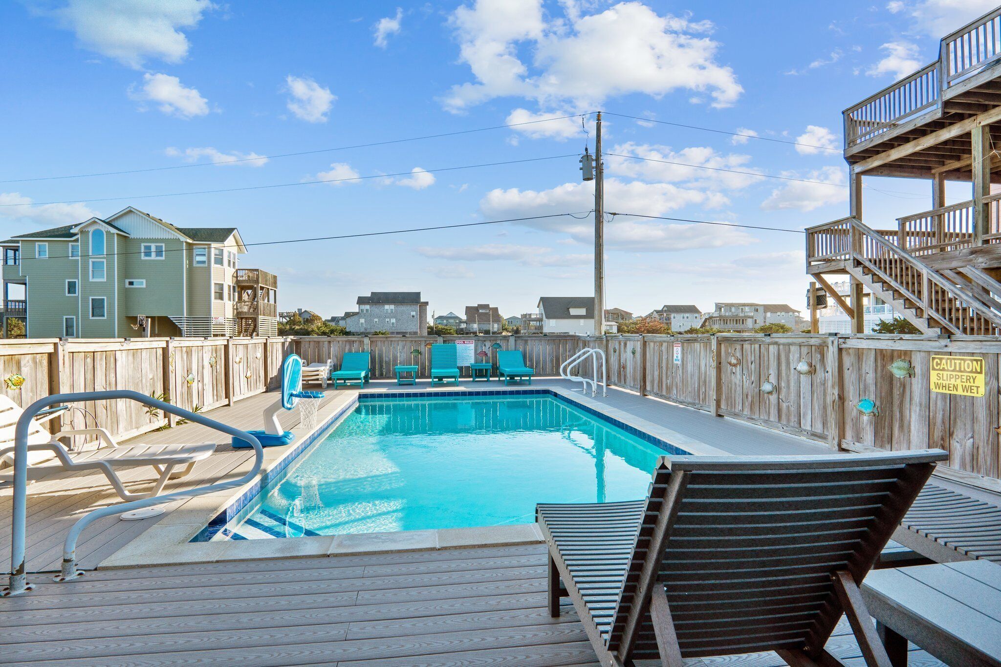 A swimming pool with wooden deck chairs and a caution sign.